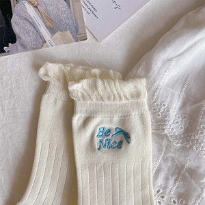Detail of cream white ribbed mid-calf socks with ruffle trim and Be Nice embroidery