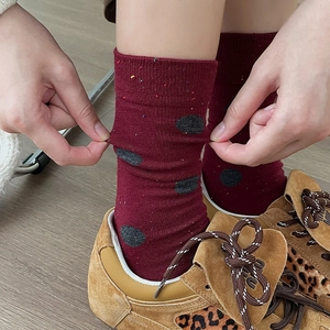 Close-up of stretchy burgundy crew socks with black polka dots and confetti knit texture