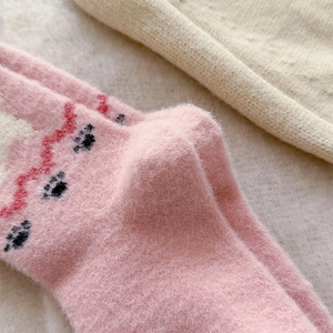 Close-up of pink fluffy knit socks featuring cute black paw prints and soft plush texture