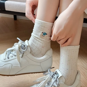 Close-up of ribbed socks with bear embroidery and colorful flecks on off-white fabric