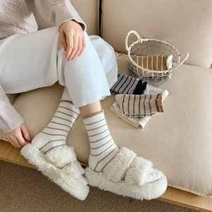 Detail of warm striped fuzzy socks paired with fluffy plush slippers in a cozy home setting