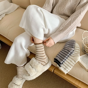 Close-up of warm striped velvet socks paired with plush white fuzzy house slippers