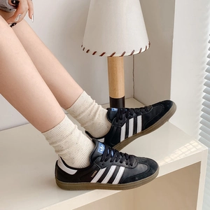 Classic Adidas Samba black leather sneakers with white stripes and gum rubber sole worn with socks