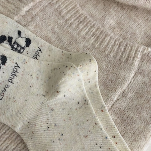 Détail de chaussette en maille beige avec broderie love puppy et texture mouchetée