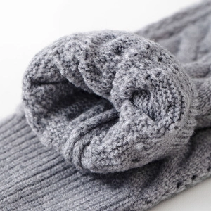 Macro detail of gray cable knit leg warmer showing intricate texture and ribbed cuff