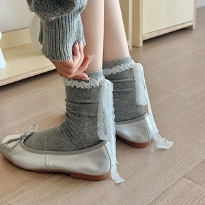 Close-up of grey lace trim socks with ribbons paired with silver ballet flats on wood floor