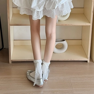 Detail of white lace ruffle socks with long ribbons and silver ballet flats on wood