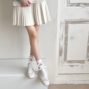 Detail of white hollow-out knee-high socks with pink bows and beige ballet flat shoes