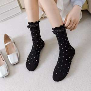 Détail de chaussettes hautes noires à pois avec bordure volantée et petit nœud