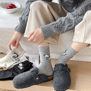 Détail de chaussettes en coton avec broderie de chiot portées avec des sabots en feutre