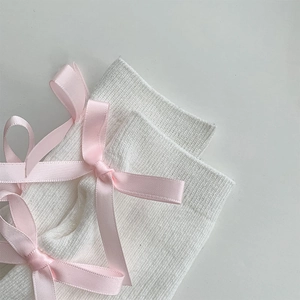 Detailed macro view of white ribbed knit socks featuring delicate pink satin bows