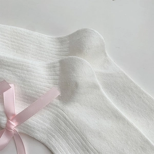 Close-up of white ribbed knit socks featuring a sweet pink satin bow detail