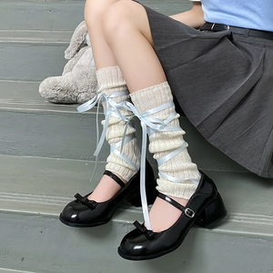 Macro detail of white ribbed knit leg warmers with crossed light blue satin ballet ribbons