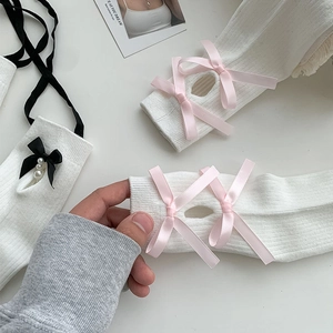Detail of white knit leg warmer with pink bows, pearls and black ribbon lacing
