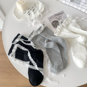 Detail of three lace crew socks with bow ribbons in black, grey, and white on a table