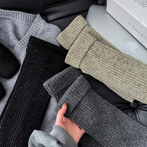 Close-up of thick speckled Donegal knit leg warmers with ribbed cuffs in three neutral colors