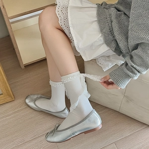 Detail of white lace trim socks with ribbons and silver ballet flats on wood floor