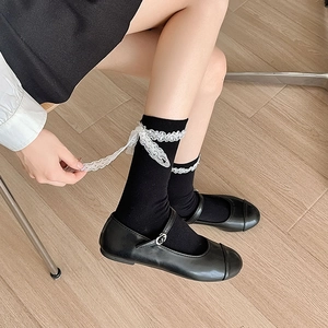 Detail of black mid-calf socks with white lace trim and bow ribbon in Lolita style