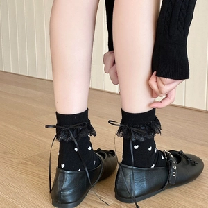 Detail of black crew socks with white hearts, lace trim and bows styled with Mary Janes