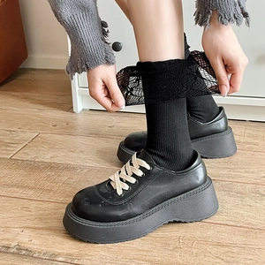 Detail of black leather platform loafers with beige laces and lace trim mesh socks