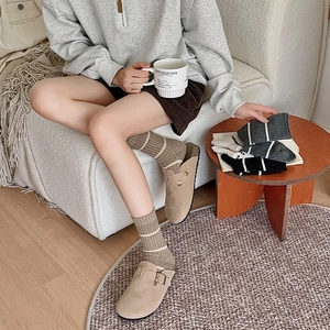 Detail of camel suede clogs and striped knit socks in a cozy minimalist home setting