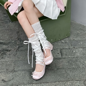 Detail of white knitted leg warmers with satin ribbons and pink ballet flats