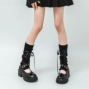 Detail of black satin ribbon bow tied on knit leg warmers with platform Mary Jane shoes