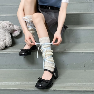 Detail of white knit leg warmers with light blue ribbons and ballet-style lace-up design