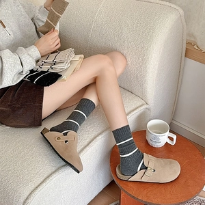 Close-up of camel suede mule slippers with buckle and striped knit socks in cozy interior