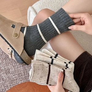 Detailed close-up of striped rib-knit cotton socks paired with suede clogs on floor