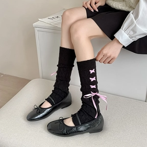 Detail of black knitted leg warmers featuring pink plaid ribbon lace-up bow and ruffles
