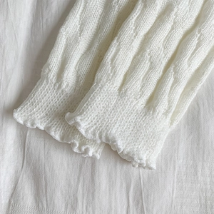 Close-up of white cable knit leg warmers with delicate ruffled edges for autumn