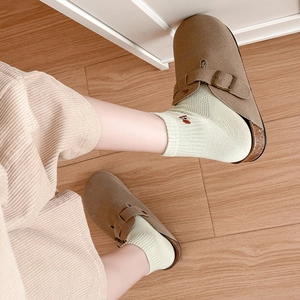 Brown suede clog mules with metal buckles and green knit socks on wooden floor