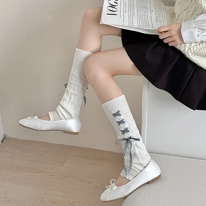 Close-up of white knitted leg warmers with lace-up bow and textured ribbed weave details