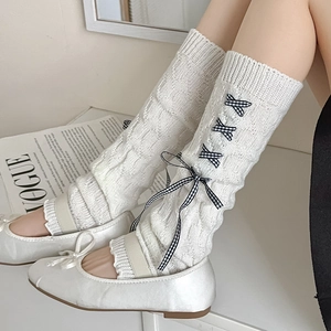 Close-up of white knit leg warmers with ribbon bows and matching ballet flats shoes