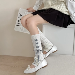 Close-up of white cable-knit leg warmers with checkered bows and ballet flats