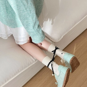 Detail of white mid-calf socks with black polka dots, ribbons, and mint green sneakers