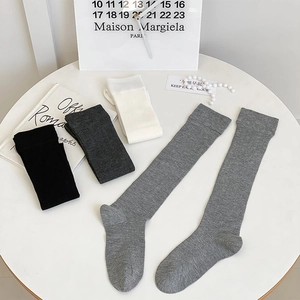 Chaussettes hautes côtelées en noir, beige et gris présentées sur une table blanche