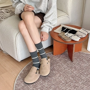 Detail of striped cotton crew socks and khaki mule shoes in a cozy home setting