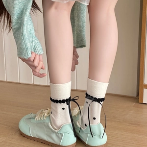 Detailed close-up of cream crew socks featuring black polka dots and velvet ribbon bows