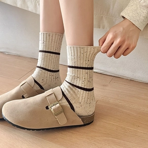 Detail of beige striped knit socks with vintage clogs on warm light wood floor