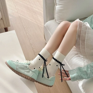 Detail of white polka dot crew socks with black bow ribbons and mint green casual shoes