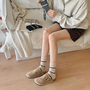 Close-up of striped cotton socks paired with khaki suede mules in a cozy setting