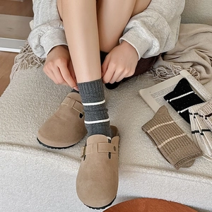 Close-up of camel suede clogs with adjustable strap paired with grey striped socks