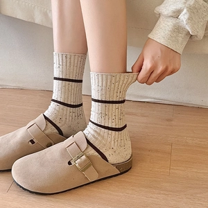 Detail of ribbed beige striped socks paired with suede mule shoes on wooden floor