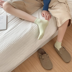Close-up of mint green ribbed cotton socks paired with brown suede loafers in a cozy room