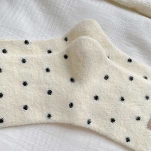 Gros plan de chaussettes pelucheuses crème à pois noirs montrant la matière thermique