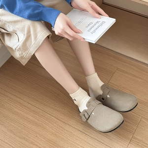 Khaki suede clogs with adjustable metal buckles and rubber soles on wooden background