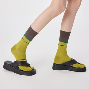 Detail view of mustard green two-toe socks with stripes worn with black flip-flops