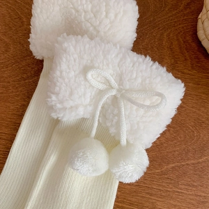 Detail of cream white leg warmers with plush faux fur, bow and small pompom accents